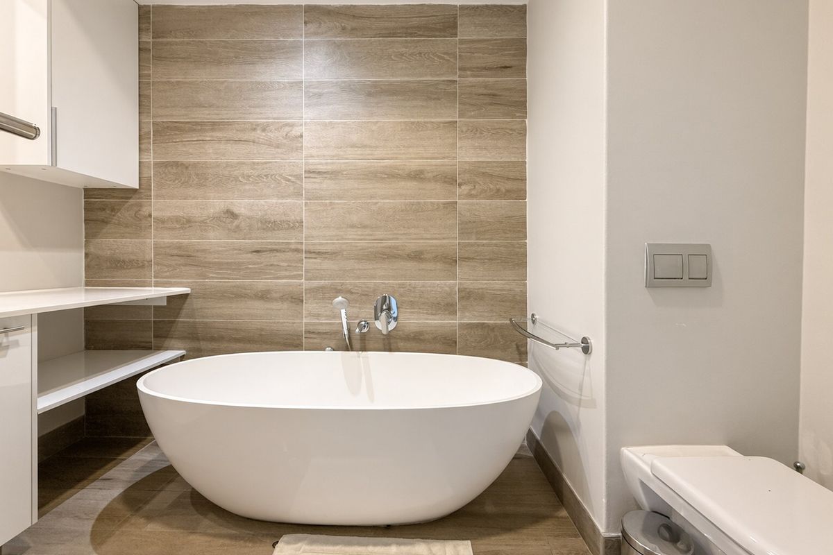 Modern bathroom featuring a sleek freestanding bathtub, wood-look tile feature wall, and integrated cabinetry with contemporary fixtures.