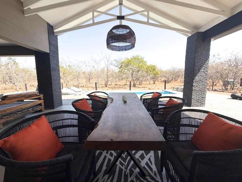 Covered outdoor patio featuring exposed truss ceilings, stacked stone columns, and direct access to the pool area with scenic bushveld views.