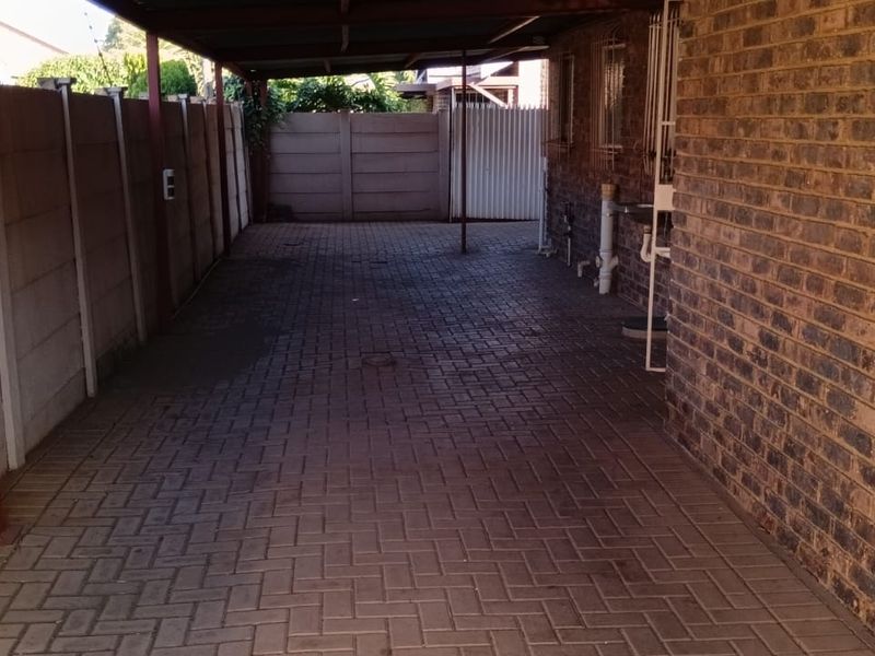 A covered carport area featuring paved flooring and brick boundary walls, providing secure off-street parking space.