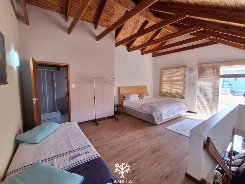 Spacious bedroom featuring high vaulted ceilings with exposed timber rafters, laminate flooring, and direct access to an en-suite bathroom.
