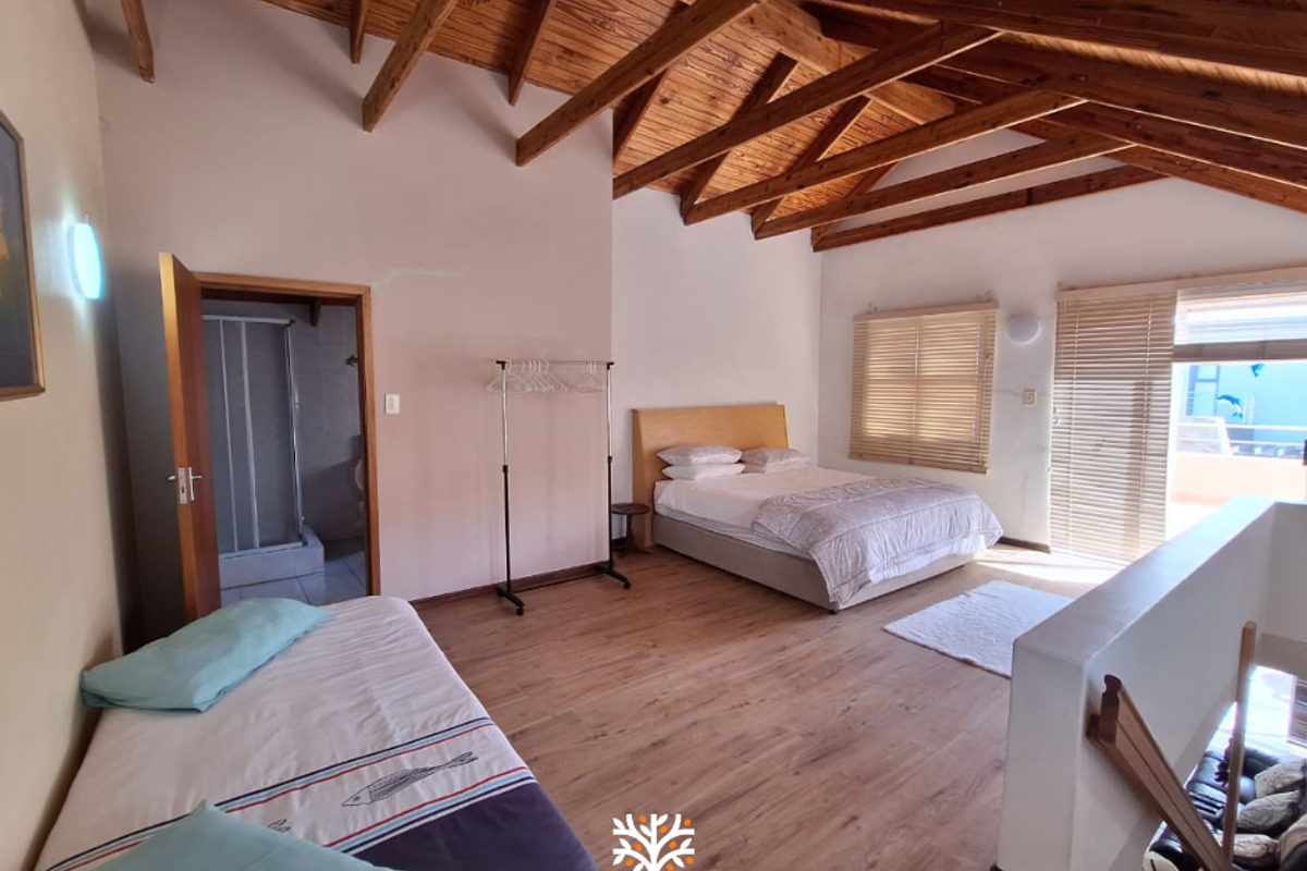 Spacious bedroom featuring high vaulted ceilings with exposed timber rafters, laminate flooring, and direct access to an en-suite bathroom.