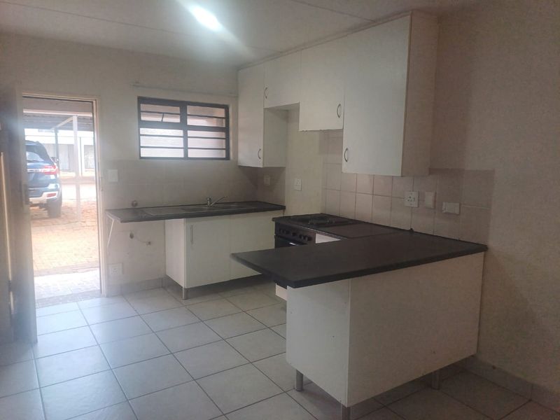 A functional kitchen featuring white cabinetry, dark laminate countertops, tiled flooring, and a freestanding stove, with direct access to the exterior.
