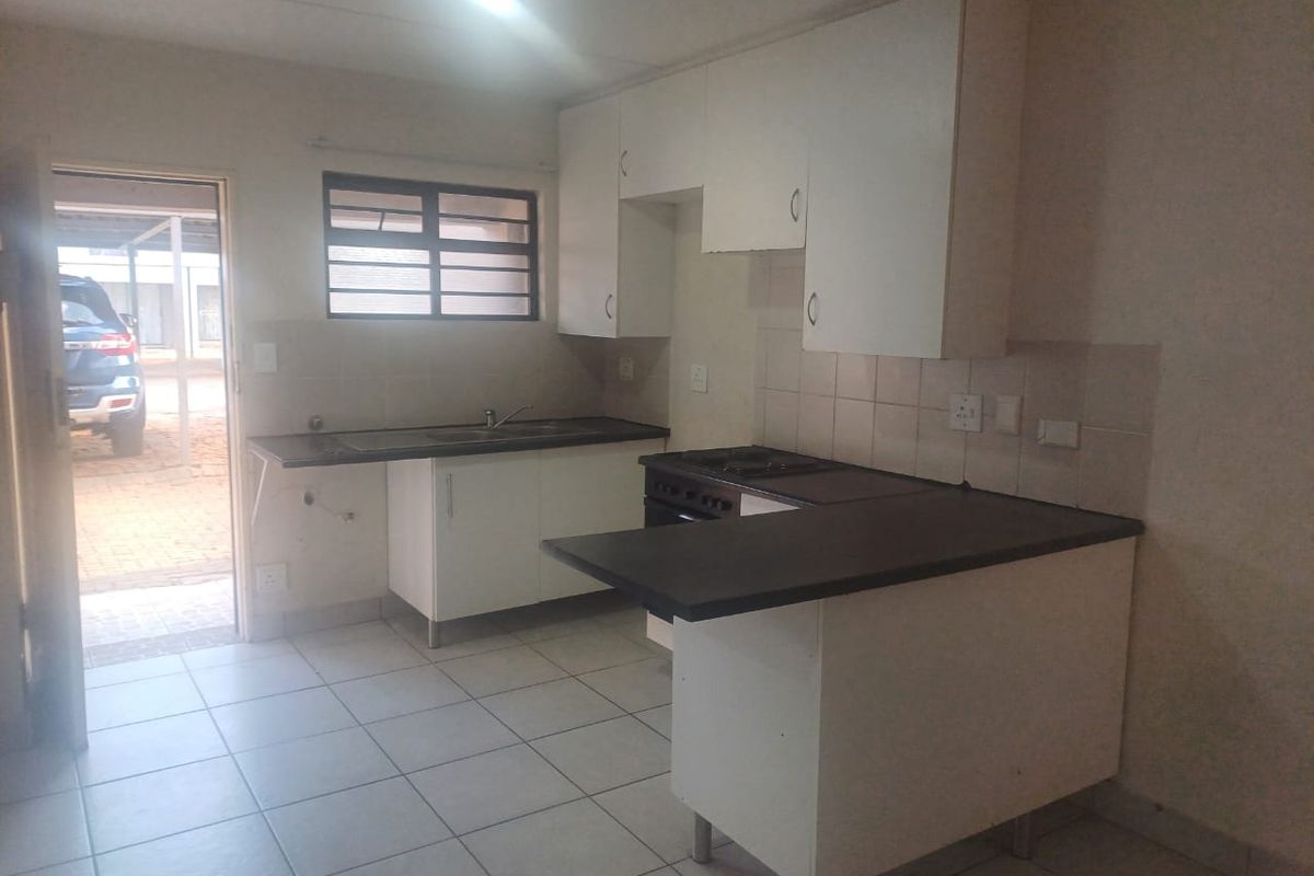 A functional kitchen featuring white cabinetry, dark laminate countertops, tiled flooring, and a freestanding stove, with direct access to the exterior.