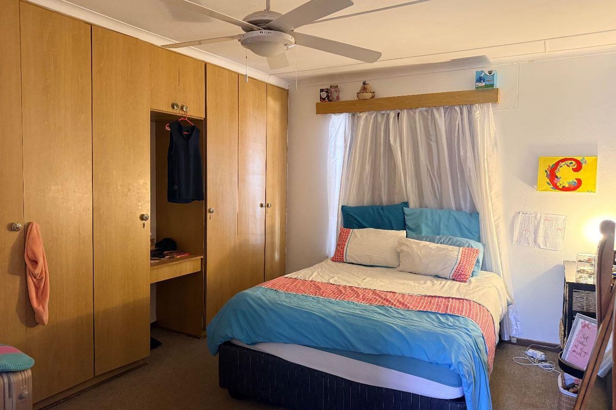 A bedroom featuring built-in wooden cabinetry with an integrated desk space, a ceiling fan, and carpeted flooring.