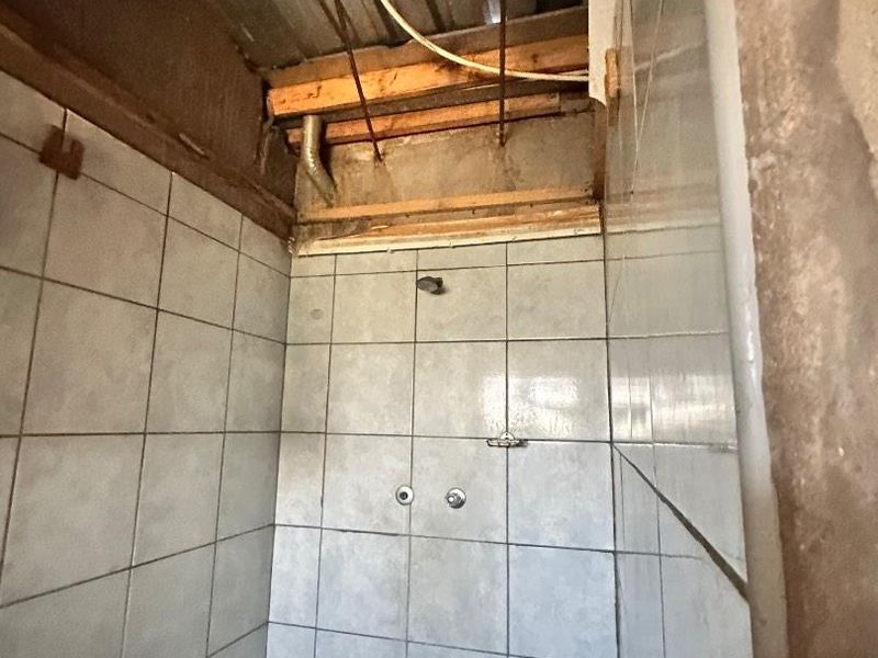 A shower enclosure featuring tiled walls, currently requiring significant ceiling and wall finishing work to complete the space.
