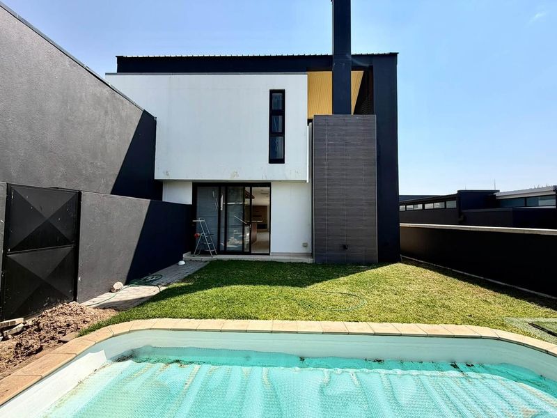Rear view of a modern townhouse featuring a private garden, swimming pool, and a contemporary two-tone facade with a prominent chimney structure.