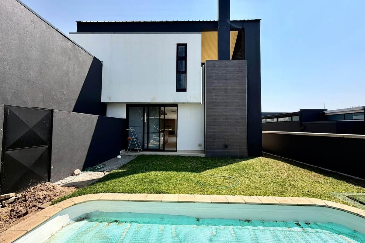 Rear view of a modern townhouse featuring a private garden, swimming pool, and a contemporary two-tone facade with a prominent chimney structure.