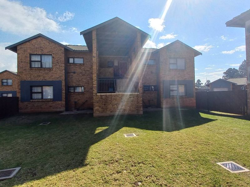 Rear view of a face brick townhouse complex featuring a shared lawn area, balconies with metal railings, and external air conditioning units.