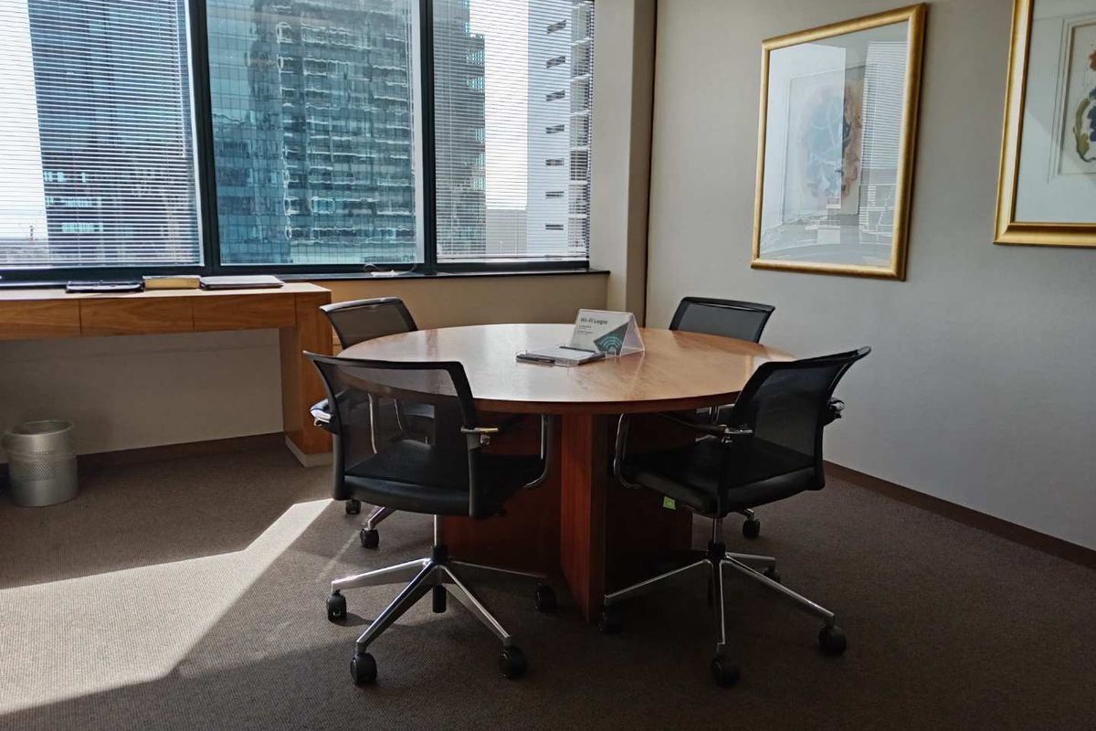 A professional office space featuring large floor-to-ceiling windows with city views, built-in wooden desk, and carpeted flooring.