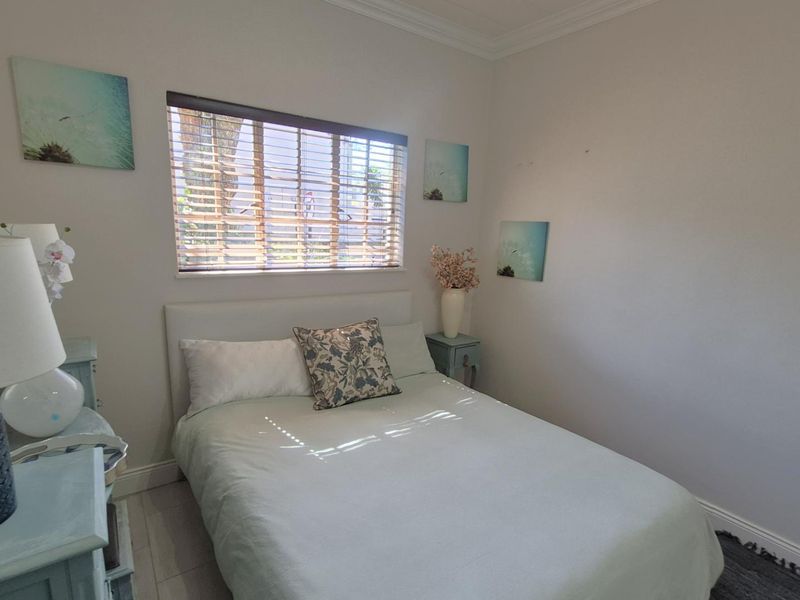 A well-maintained bedroom featuring neutral wall tones, tiled flooring, crown molding, and venetian blinds for adjustable natural light.