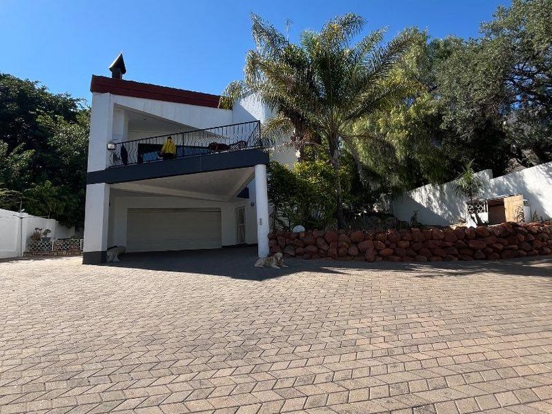 Front view of a multi-level house featuring a paved driveway, integrated garage, and an upper-level balcony with metal railings.