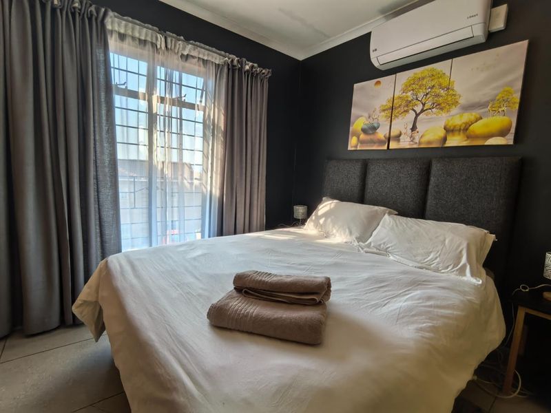 A well-maintained bedroom featuring dark accent walls, tiled flooring, and a wall-mounted air conditioning unit, providing a comfortable and modern living space.