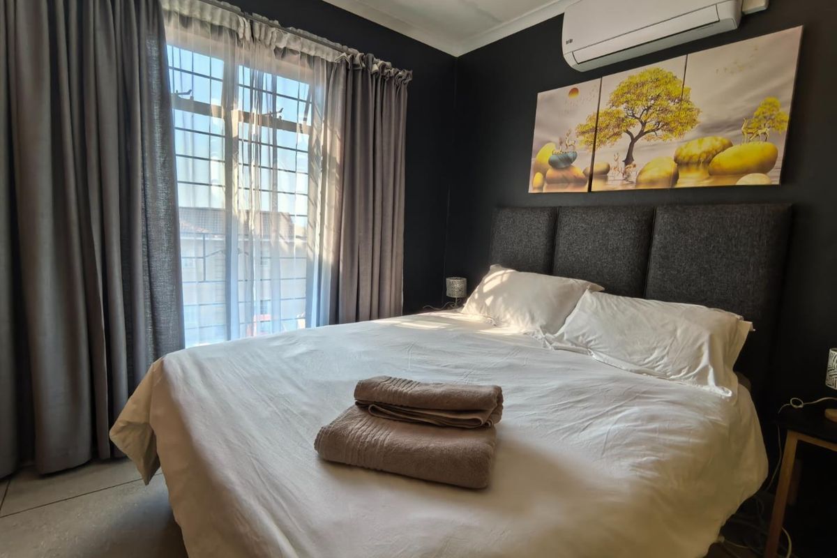 A well-maintained bedroom featuring dark accent walls, tiled flooring, and a wall-mounted air conditioning unit, providing a comfortable and modern living space.