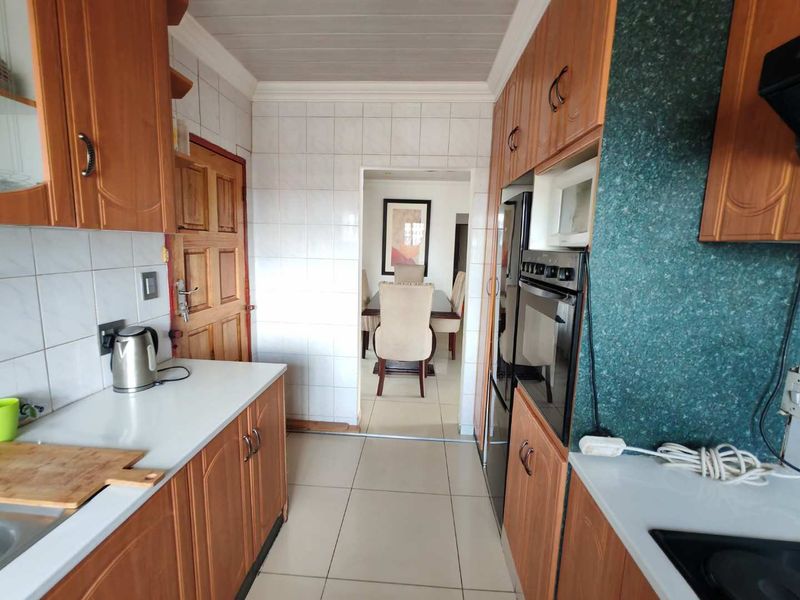 A functional kitchen featuring traditional wooden cabinetry, built-in oven and microwave, tiled backsplash, and neutral floor tiles, leading into the dining area.