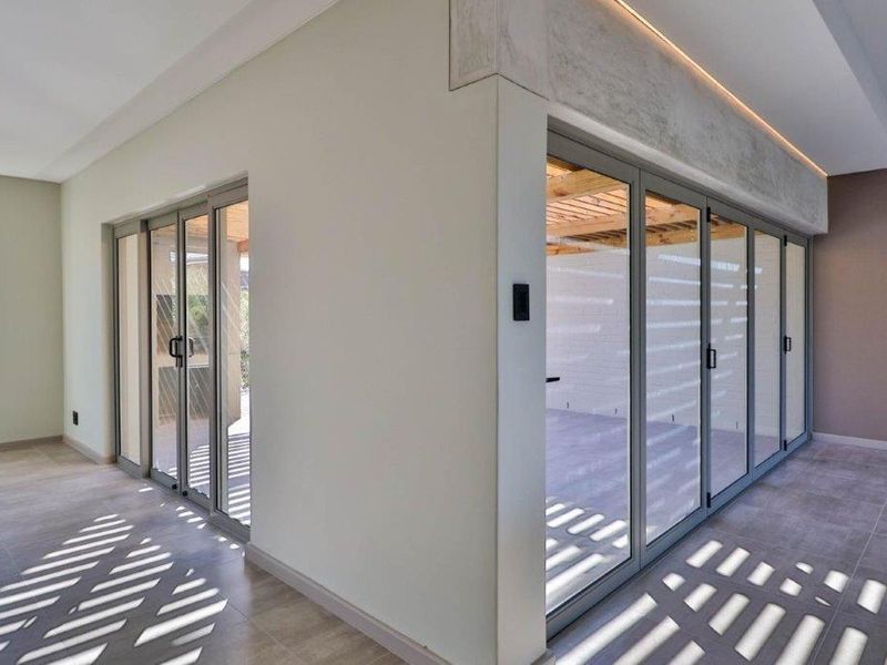 Modern living area featuring expansive aluminium stacking doors that open onto an outdoor patio, complemented by recessed ceiling lighting and neutral tiled flooring.
