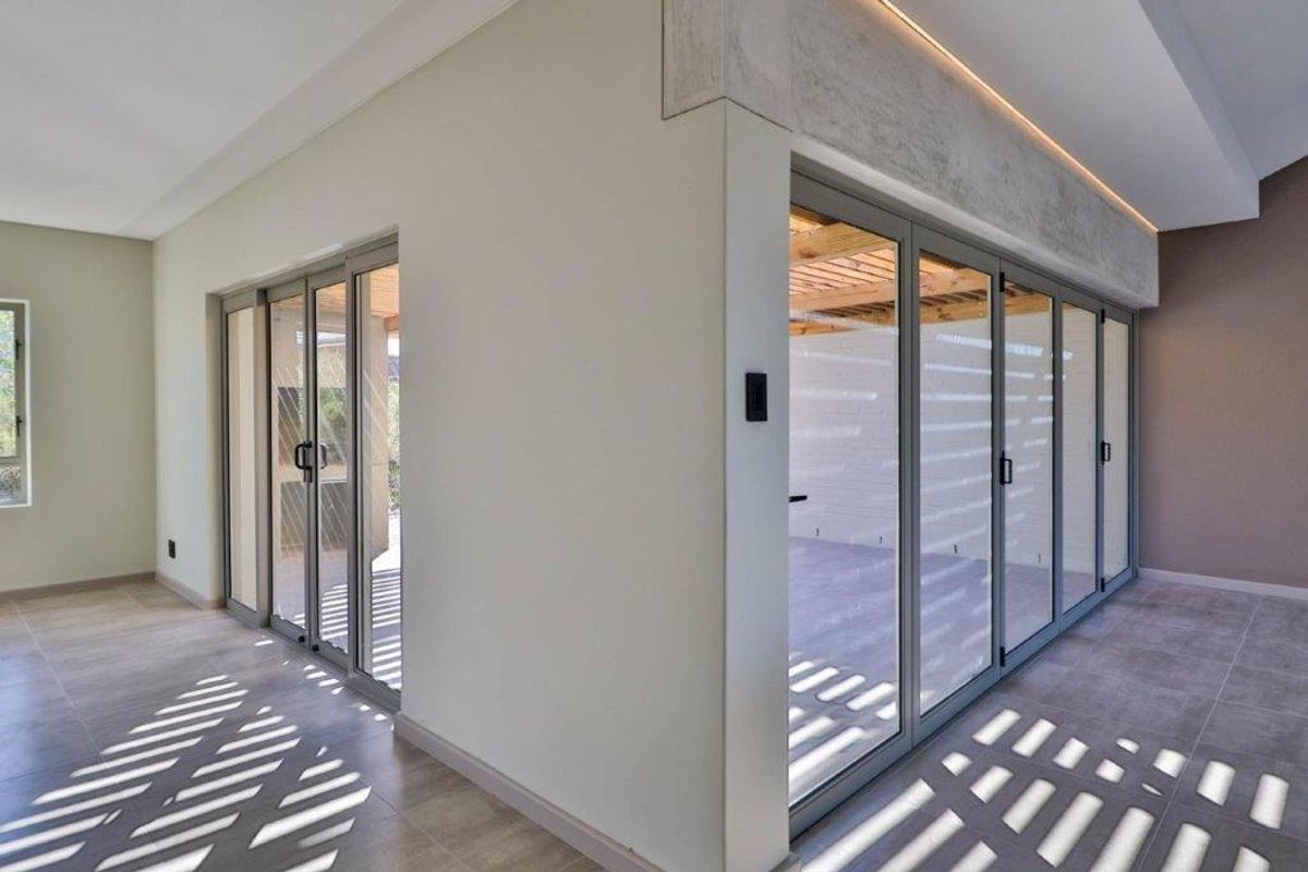 Modern living area featuring expansive aluminium stacking doors that open onto an outdoor patio, complemented by recessed ceiling lighting and neutral tiled flooring.