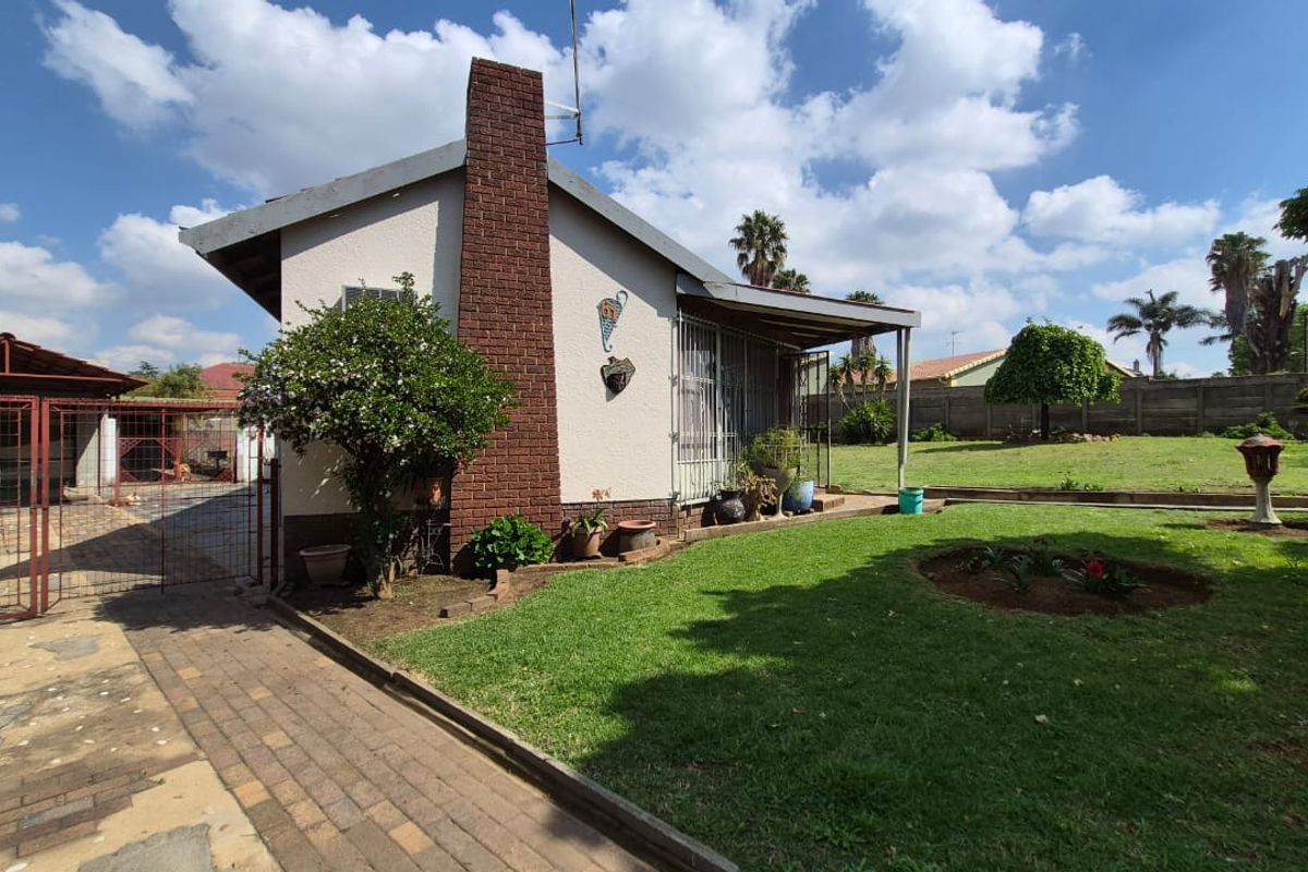 Rear view of the property featuring a brick chimney, covered patio area, paved driveway, and a spacious garden with perimeter walling.