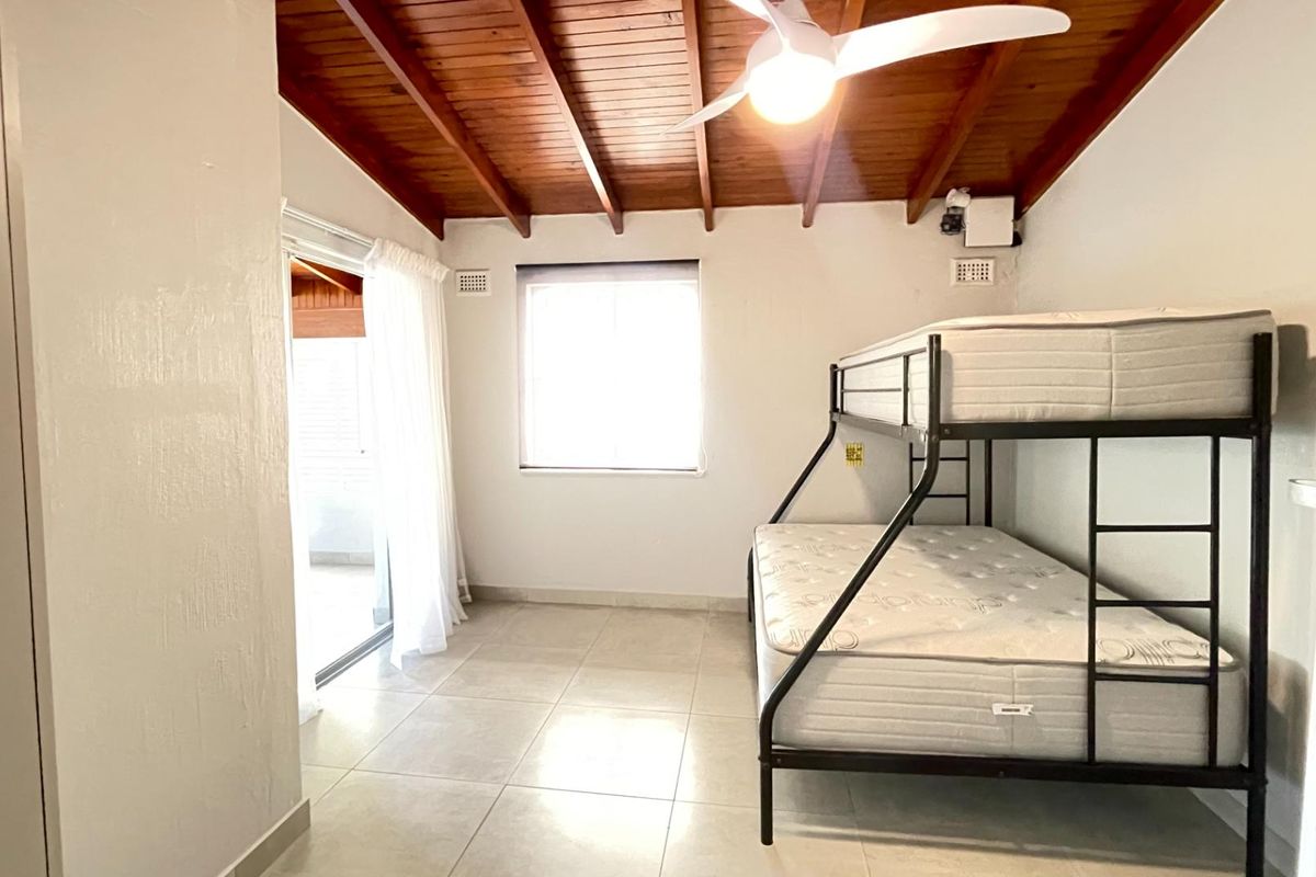 A bedroom featuring an exposed timber beam ceiling, ceiling fan, tiled flooring, and a sliding glass door providing access to an outdoor area.