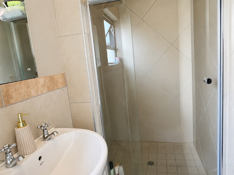 A functional bathroom featuring a pedestal basin with chrome mixer taps and a glass-enclosed shower with neutral wall tiling.