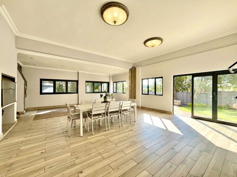 Spacious open-plan living and dining area featuring wood-look tile flooring, modern black-framed windows, and seamless access to the garden through large sliding glass doors.