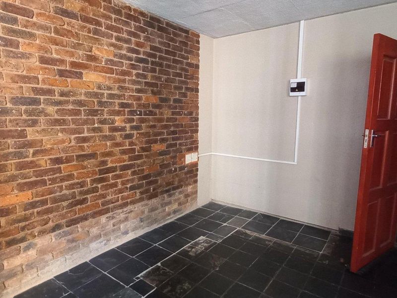 An empty living area featuring an exposed brick feature wall, dark slate tile flooring, and a secure entrance door.