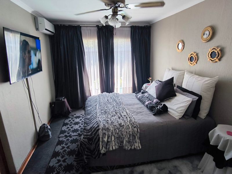 A comfortable bedroom featuring a ceiling fan, split-system air conditioning unit, and large windows with curtain tracks.