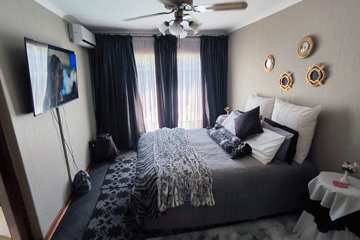 A comfortable bedroom featuring a ceiling fan, split-system air conditioning unit, and large windows with curtain tracks.