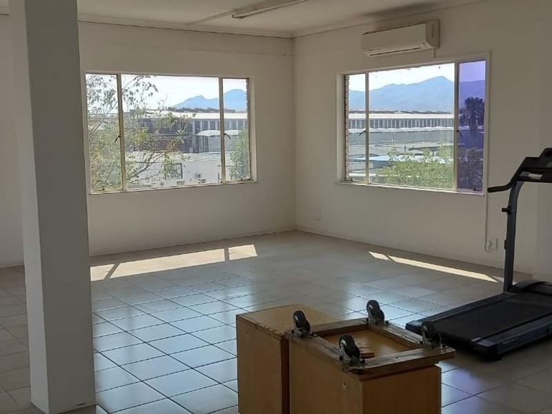 Spacious office area featuring tiled flooring, large windows providing natural light, and a wall-mounted air conditioning unit.