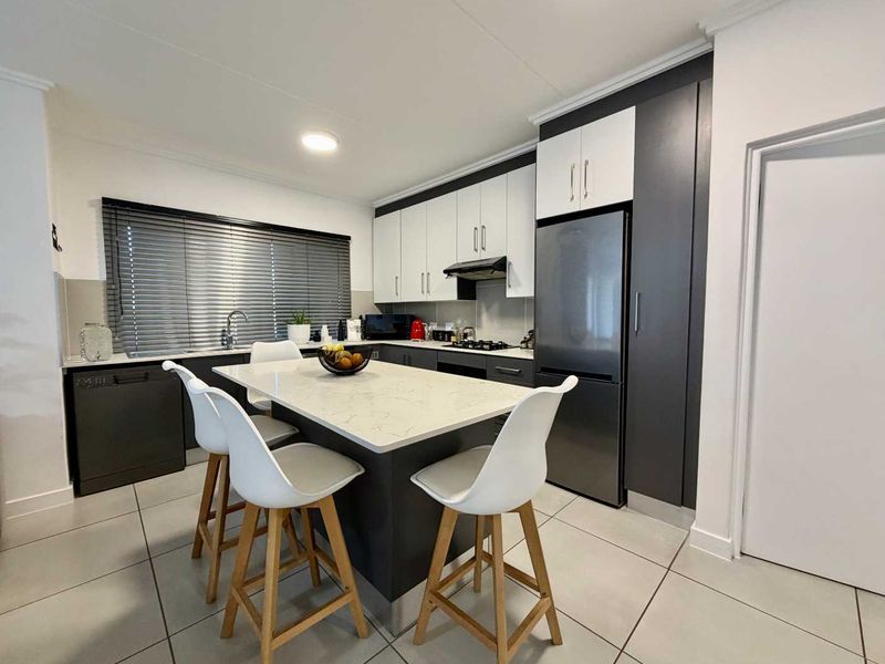 Modern kitchen featuring a central island with quartz countertop, sleek two-tone cabinetry, integrated appliances, and tiled flooring.