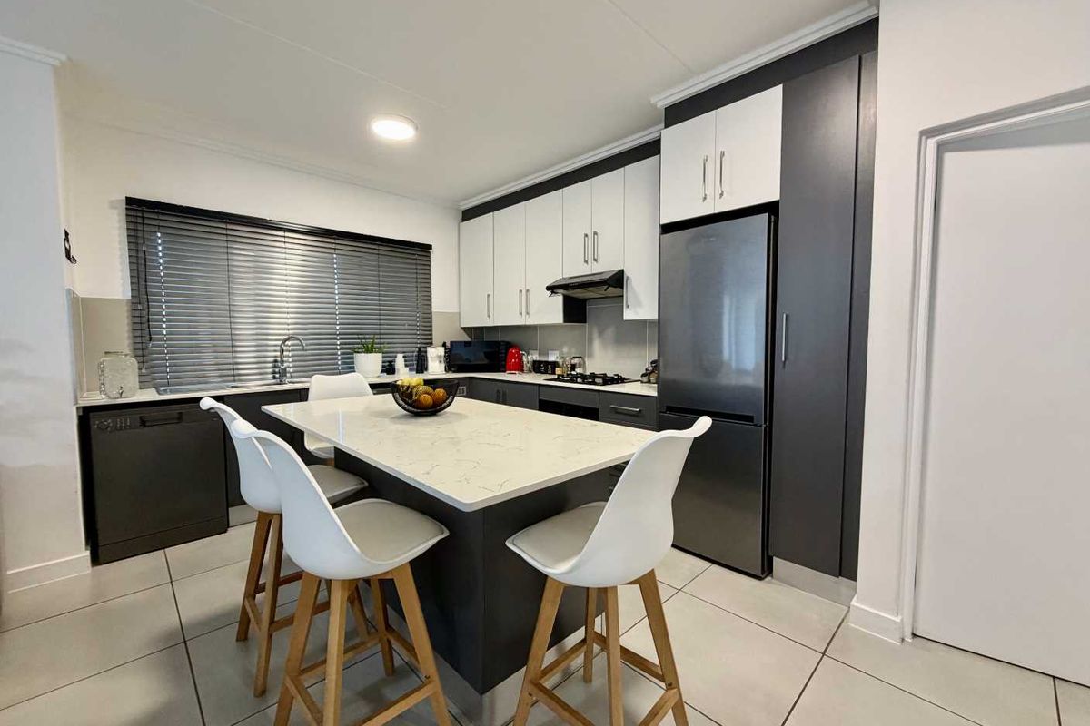 Modern kitchen featuring a central island with quartz countertop, sleek two-tone cabinetry, integrated appliances, and tiled flooring.