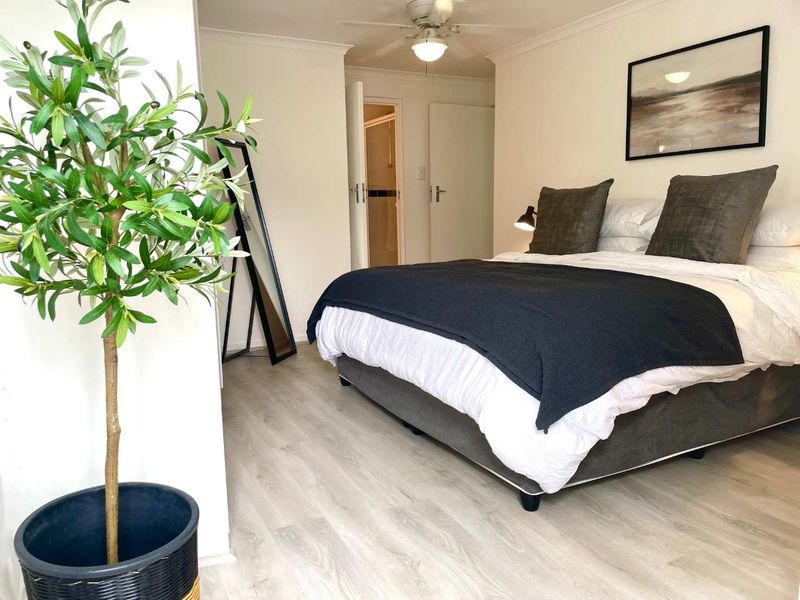A well-maintained bedroom featuring light-toned laminate flooring, a ceiling fan, and neutral wall finishes, providing a clean and comfortable living space.