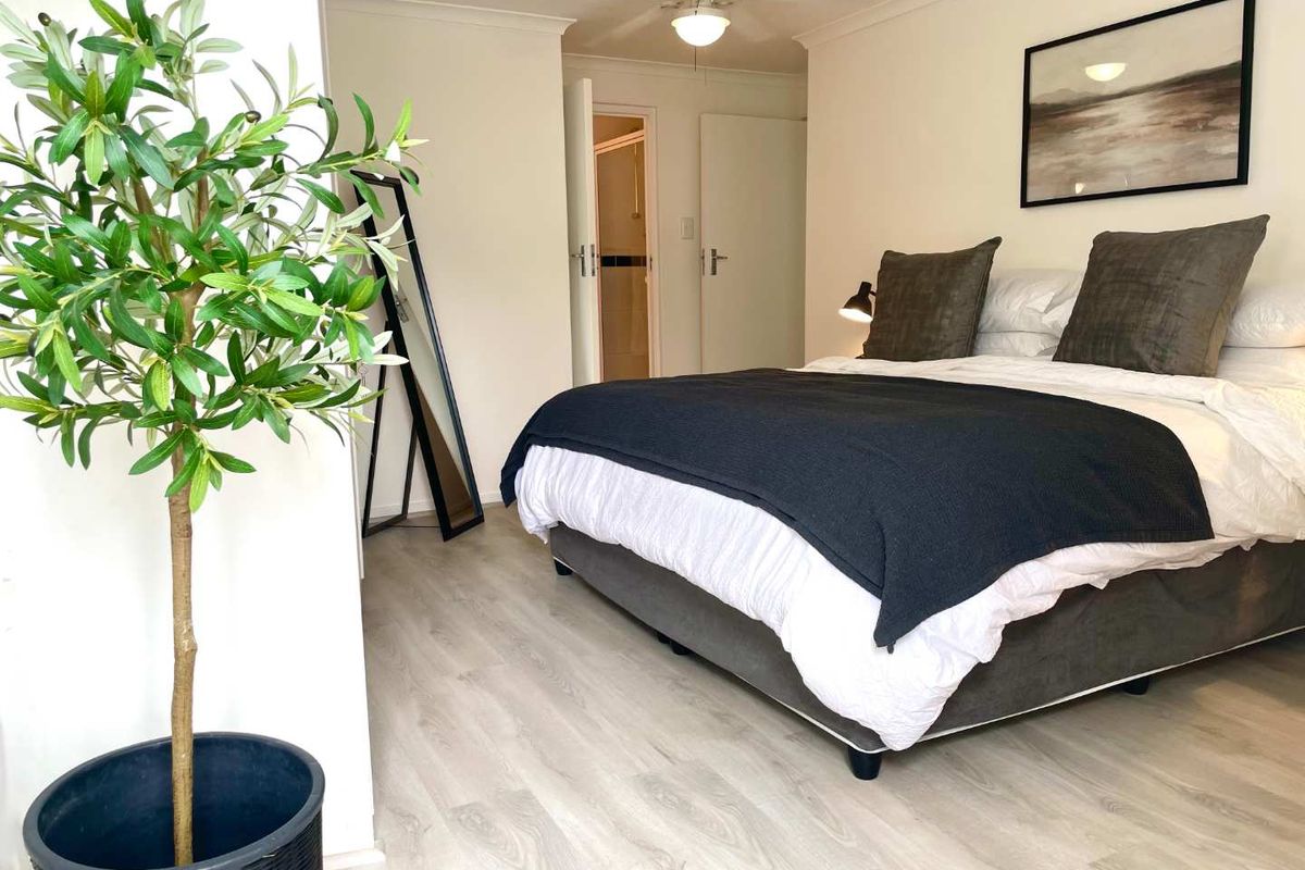 A well-maintained bedroom featuring light-toned laminate flooring, a ceiling fan, and neutral wall finishes, providing a clean and comfortable living space.