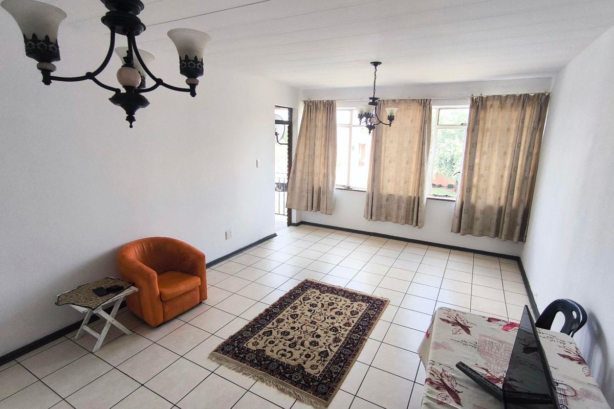 A spacious living area featuring neutral tiled flooring, large windows allowing natural light, and classic chandelier lighting fixtures.