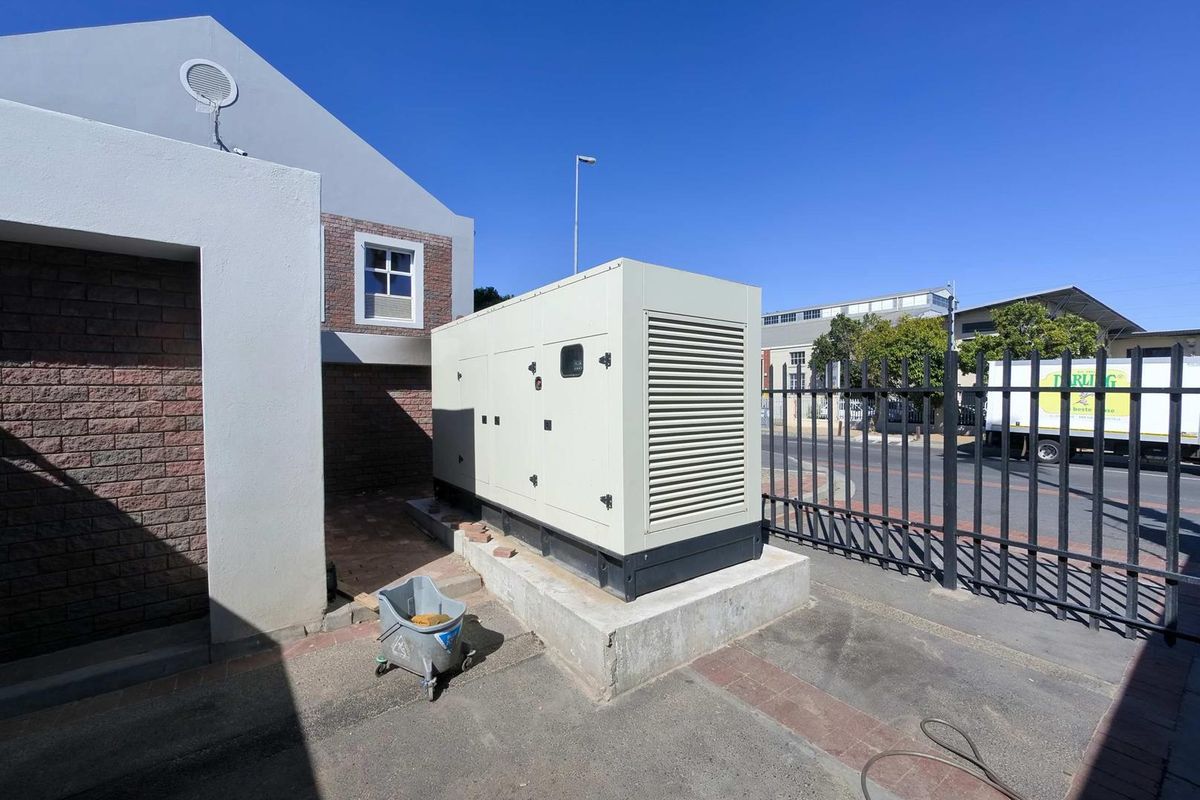 Exterior view of the property featuring a large industrial backup generator mounted on a concrete plinth, secured by perimeter metal fencing.