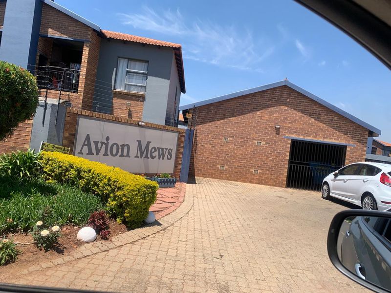 Front entrance view of Avion Mews townhouse complex featuring brick facade, paved driveway, and secure gated access.