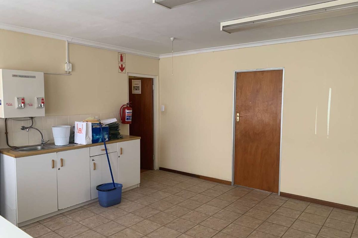 A functional office kitchenette area featuring built-in cabinetry, a sink, a wall-mounted water heater, and tiled flooring.