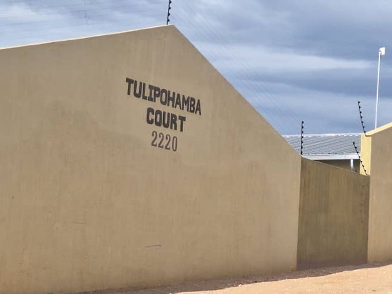 Front exterior view of Tulipohamba Court, featuring a secure perimeter wall with electric fencing and a metal entrance gate.