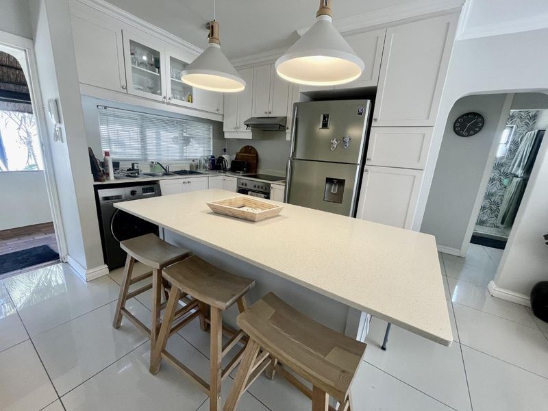 Modern kitchen featuring white cabinetry, stone countertops, a central island with breakfast bar, and integrated appliances, finished with sleek tiled flooring.