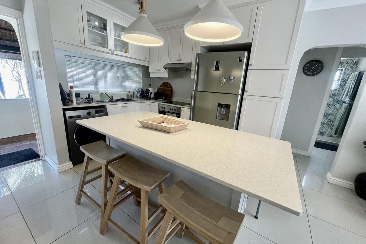 Modern kitchen featuring white cabinetry, stone countertops, a central island with breakfast bar, and integrated appliances, finished with sleek tiled flooring.