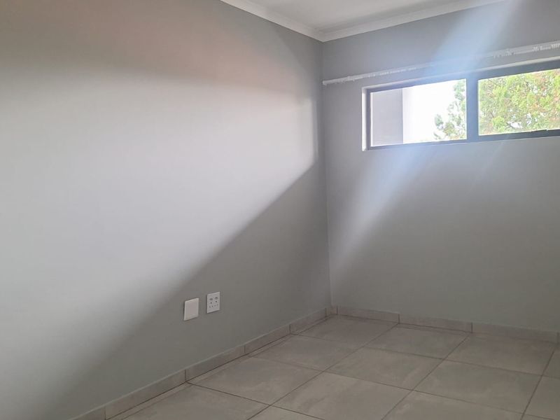 A clean, empty bedroom featuring neutral grey walls, tiled flooring, and a horizontal window providing natural light.