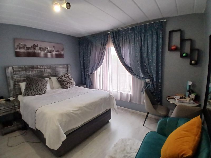 A well-proportioned bedroom featuring light-toned laminate flooring, a panelled ceiling, and ample natural light through large window treatments.