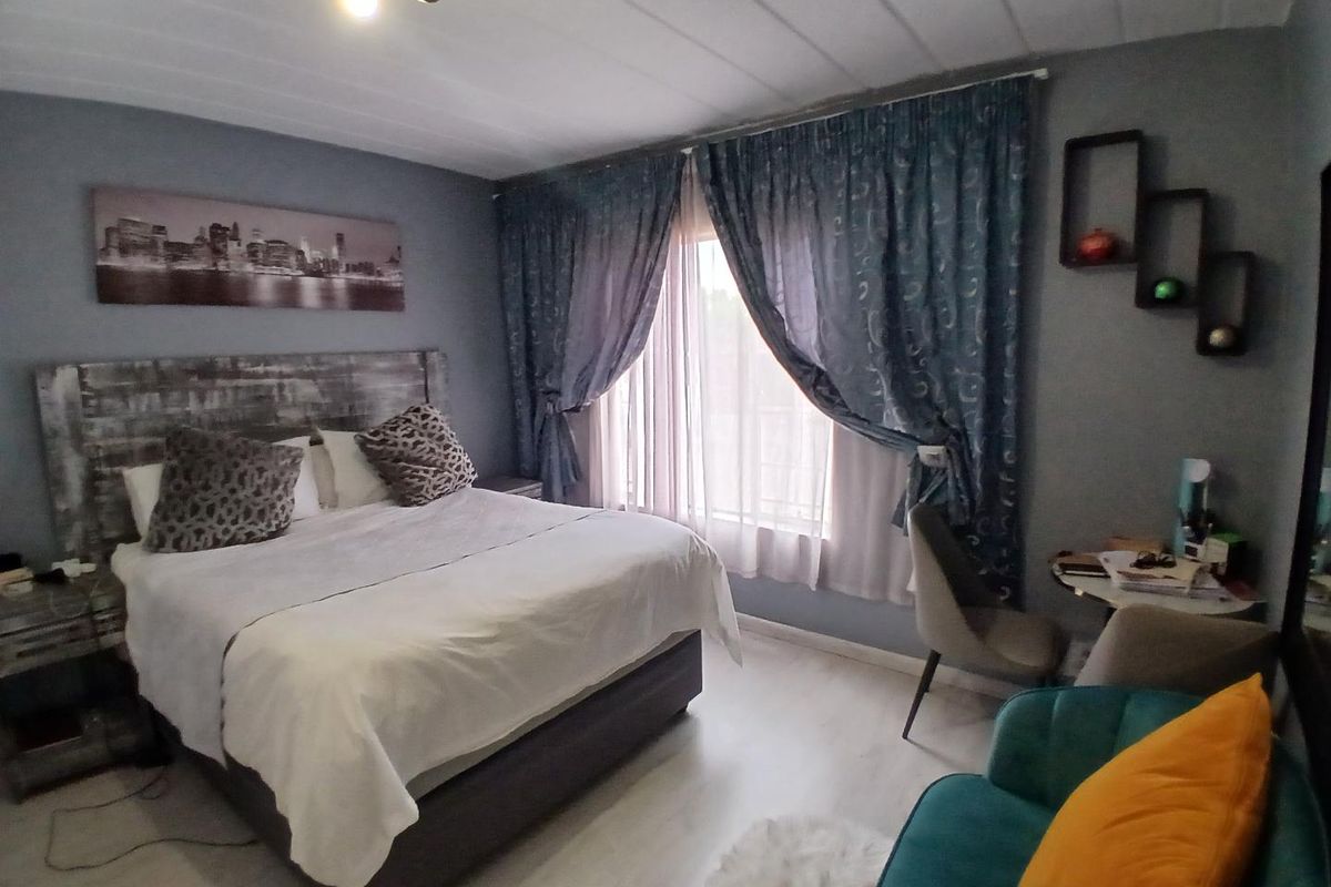 A well-proportioned bedroom featuring light-toned laminate flooring, a panelled ceiling, and ample natural light through large window treatments.