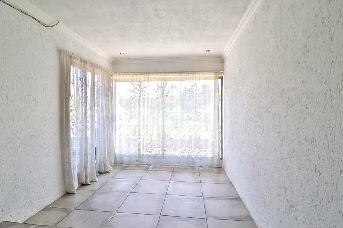 A bright, empty living space featuring large windows with natural light, tiled flooring, and textured walls, offering a versatile area for relaxation.