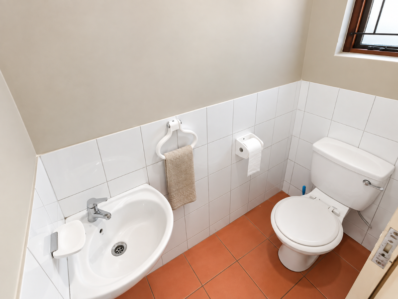 A clean and functional guest bathroom featuring a white ceramic basin, matching toilet, and neutral wall and floor tiling.