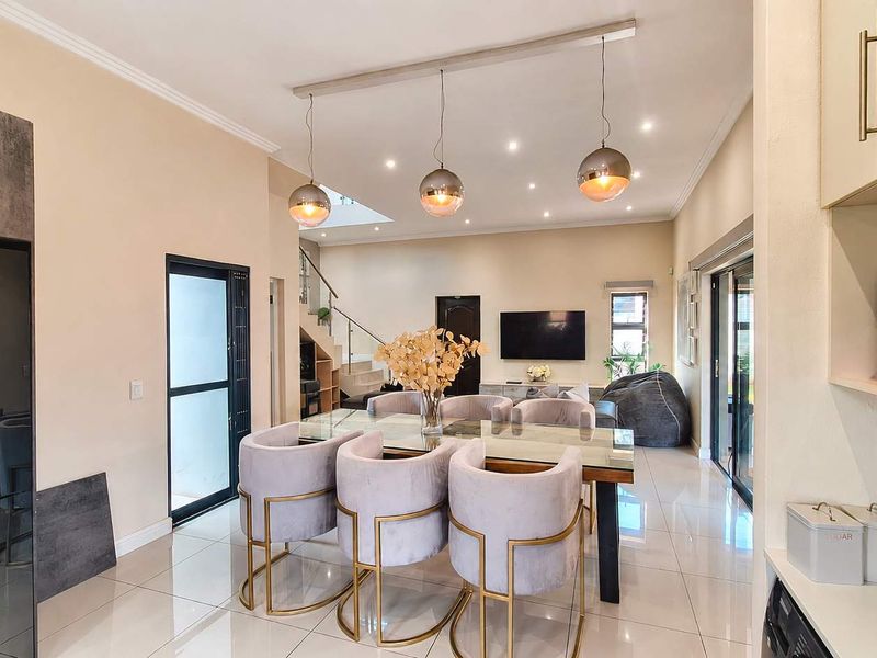 A modern open-plan living and dining area featuring sleek porcelain tiles, contemporary pendant lighting, and a staircase with a glass balustrade.