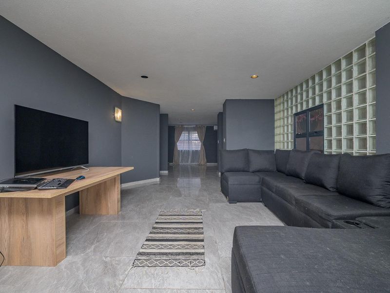 Spacious living room featuring modern dark grey walls, large format tiled flooring, and a distinctive glass block feature wall.