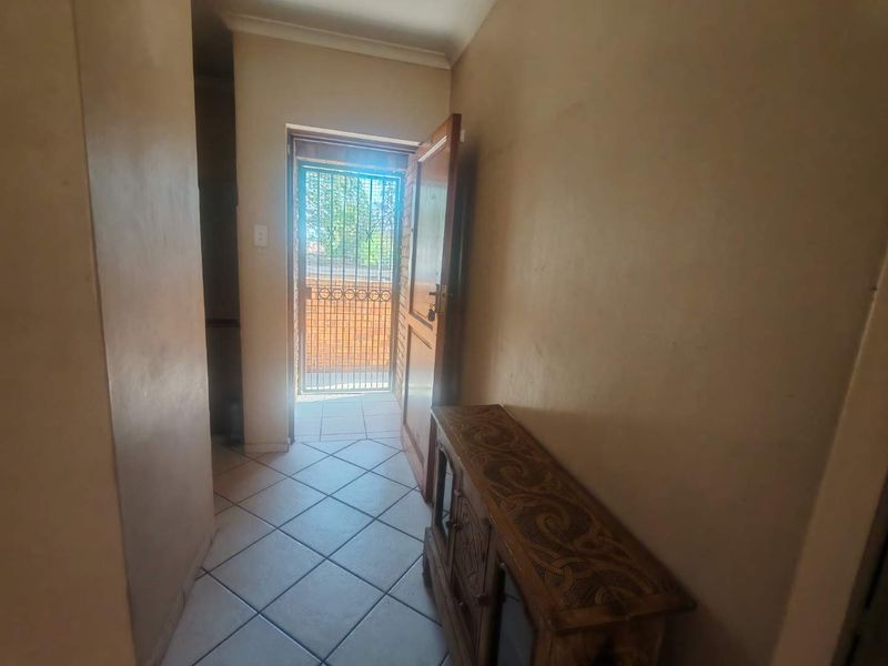 An entry hallway featuring tiled flooring, a timber door, and a security gate leading to the exterior.