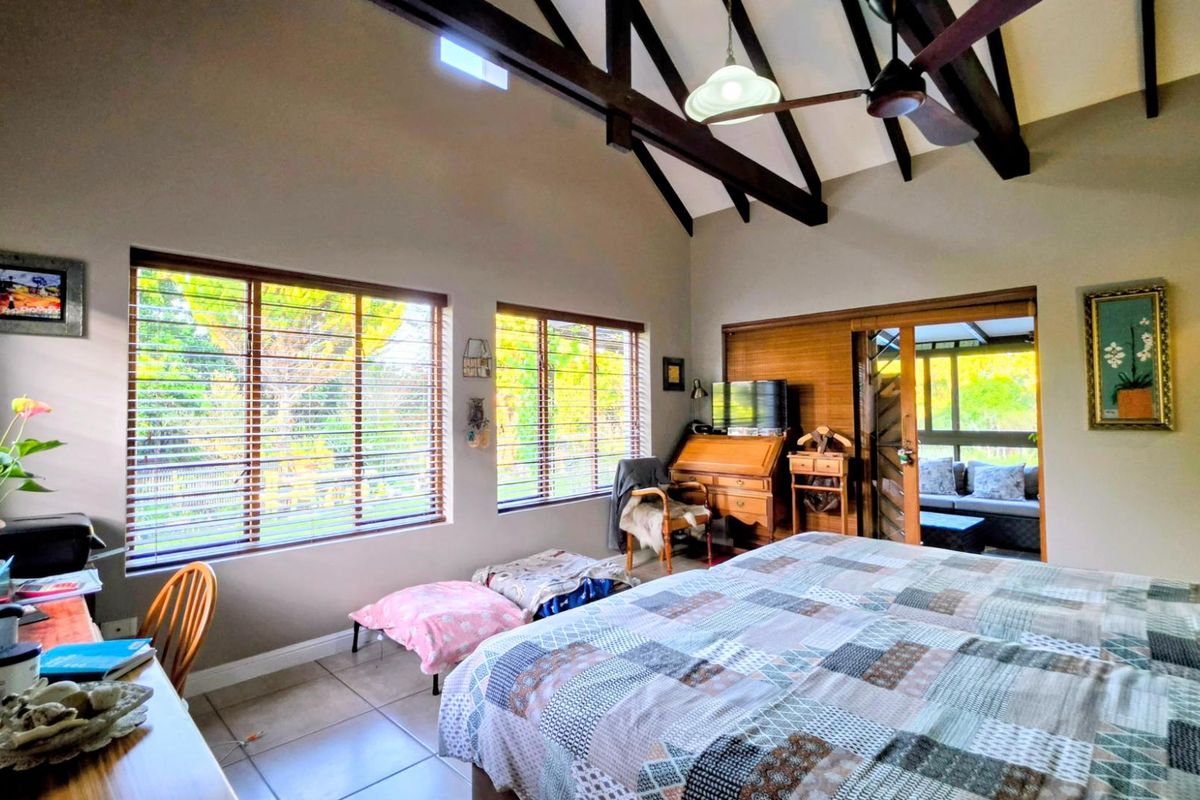 Spacious bedroom featuring high vaulted ceilings with exposed timber trusses, tiled flooring, and large windows providing ample natural light and garden views.