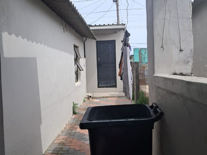 A narrow paved side passage or rear exterior area featuring a corrugated roof covering and access to an external door.