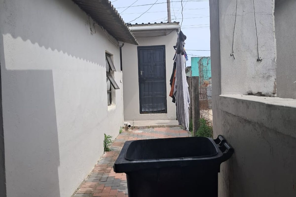 A narrow paved side passage or rear exterior area featuring a corrugated roof covering and access to an external door.
